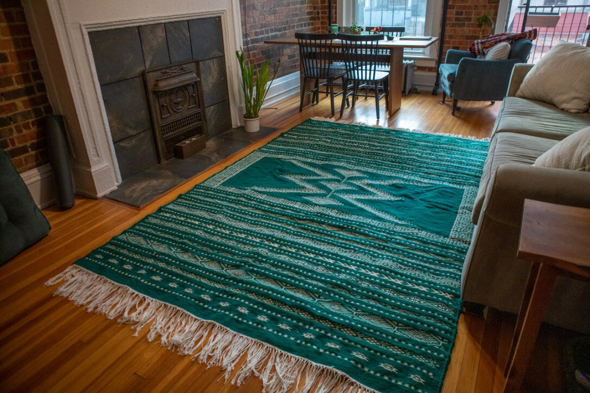 Green area rug with white patterns and long fringe