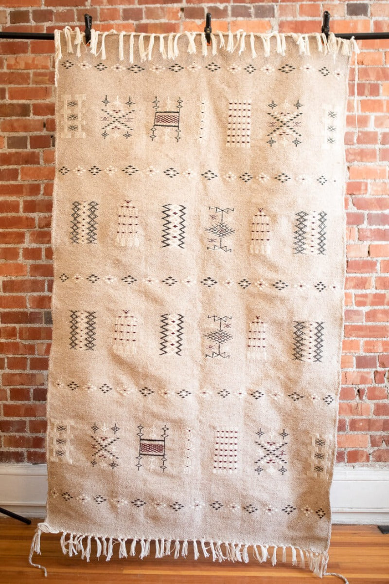 Gray berber rug with traditional geometric motifs. Handwoven in Algeria. With brick wall in the background