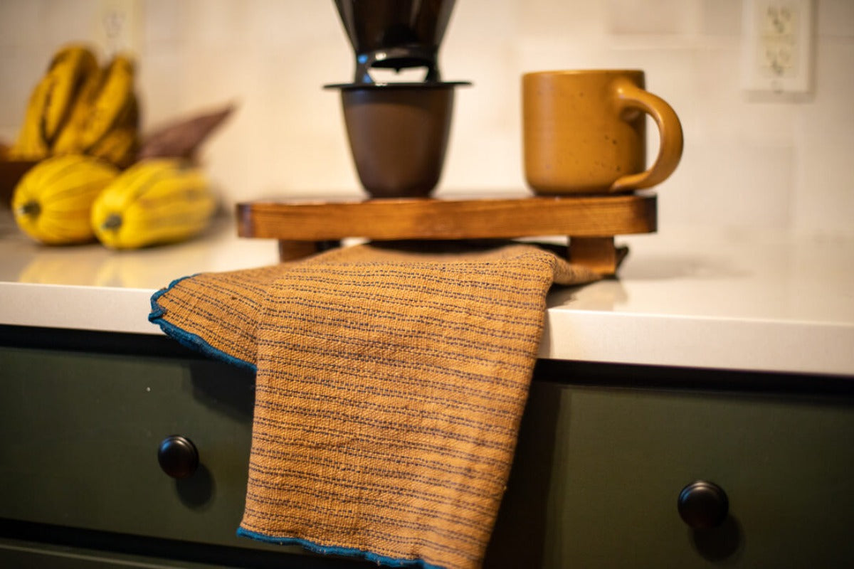 Kitchen towel with blue lining on countertop with coffee set up.