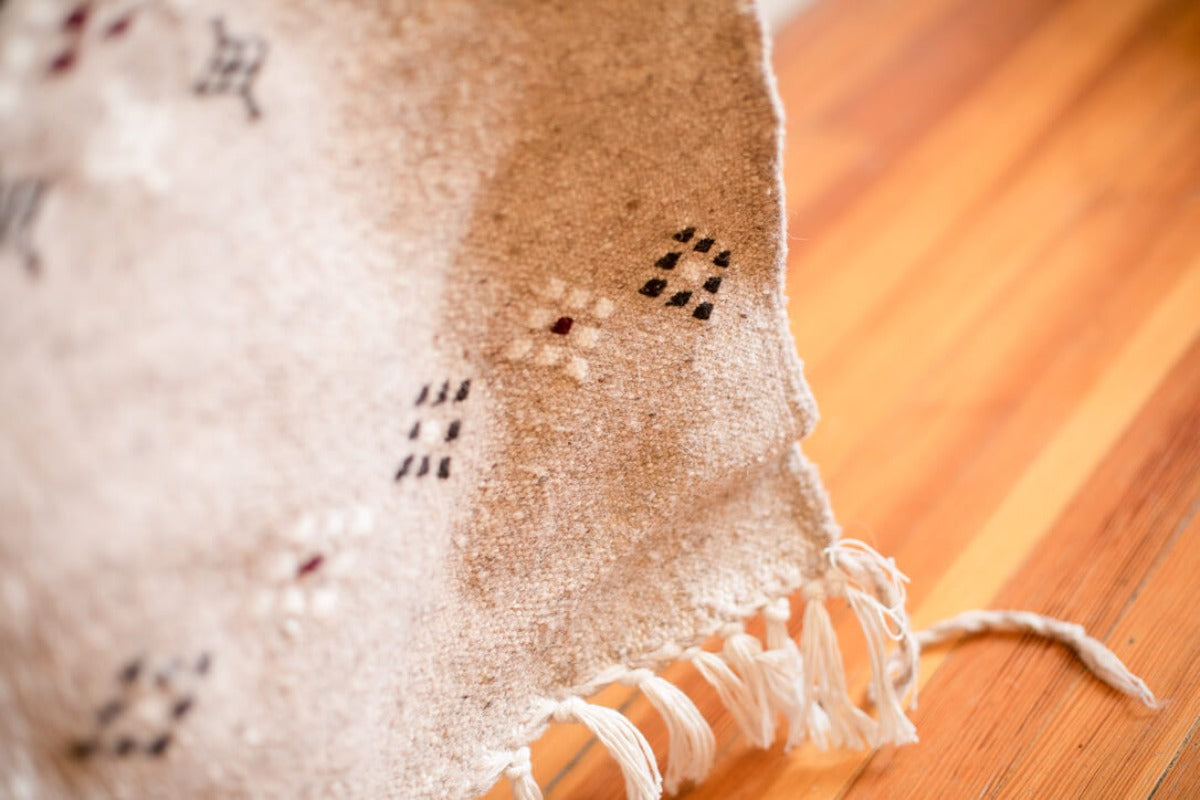 Close up of gray rug with traditional geometric motifs and tassels. 